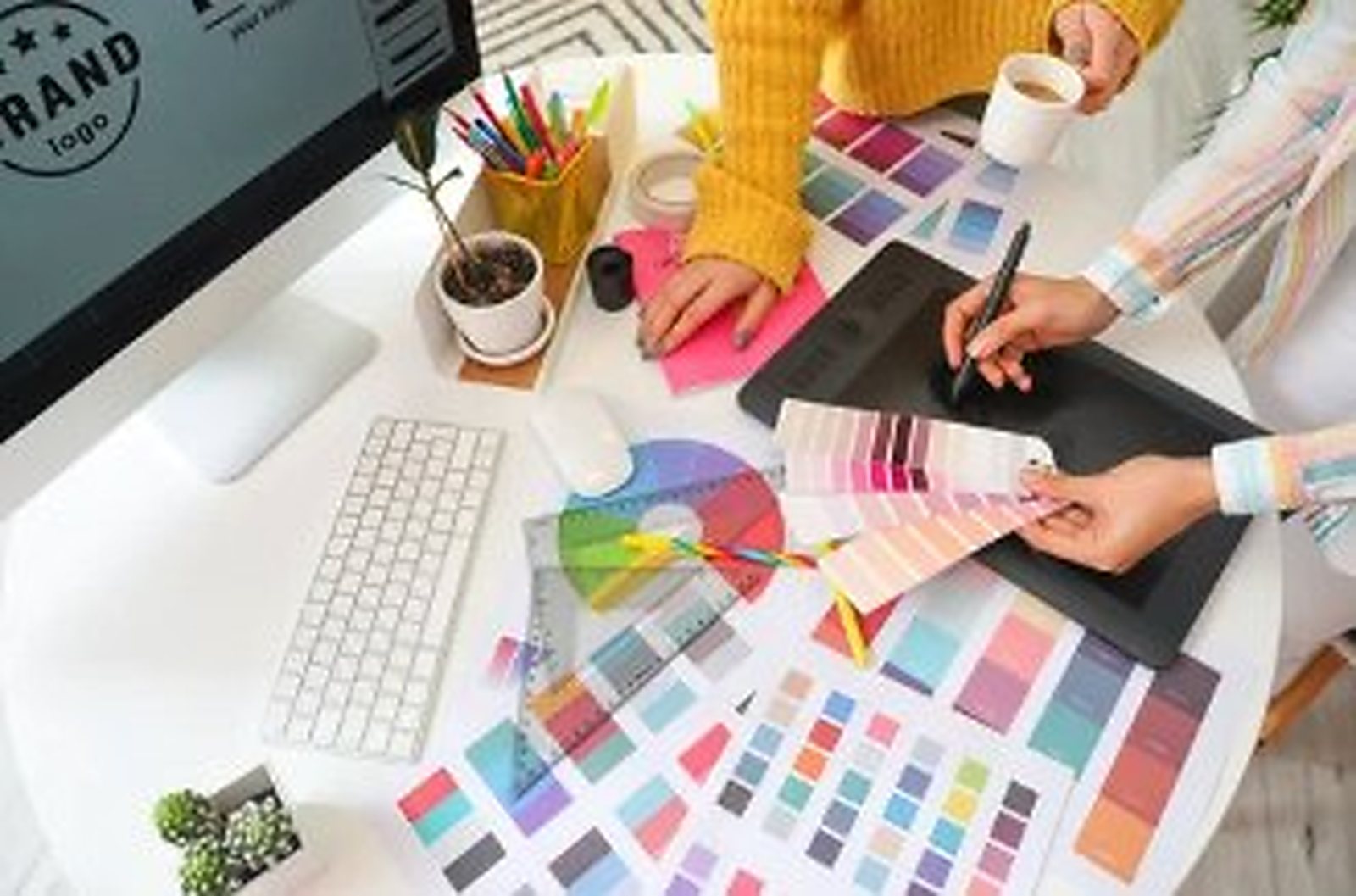Two designers working over colour swatch fans, printed palettes and a graphics tablet.