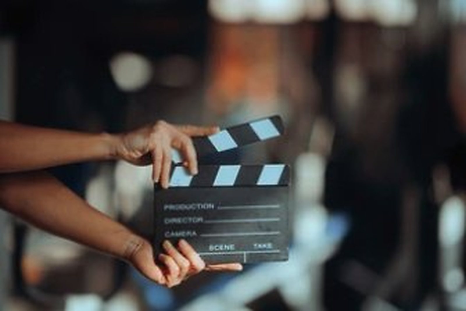 Hands holding a film clapperboard in front of out-of-focus set lights.