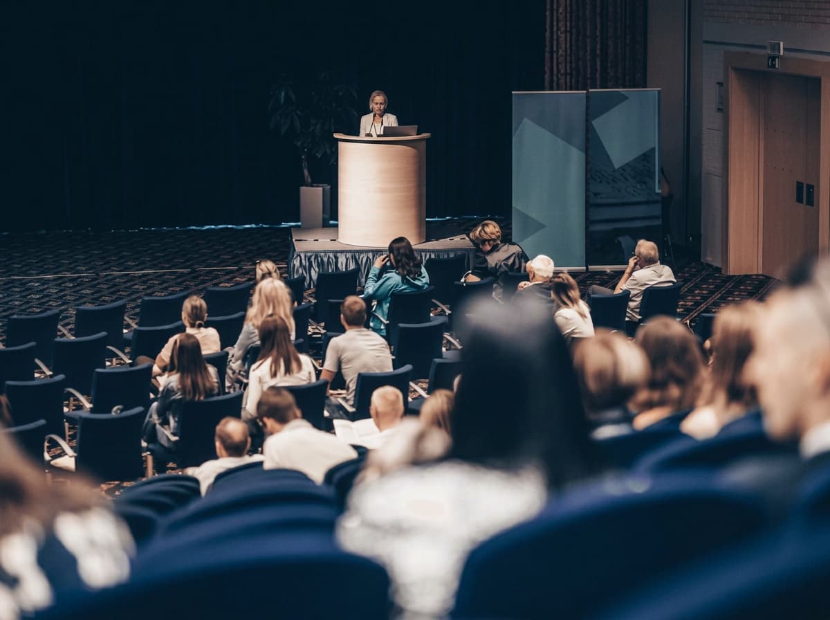 A speaker addressing a seated audience from a lectern in a university hall.