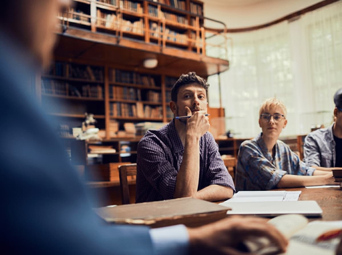 A student thinking at a desk in a wood-panelled reading room.