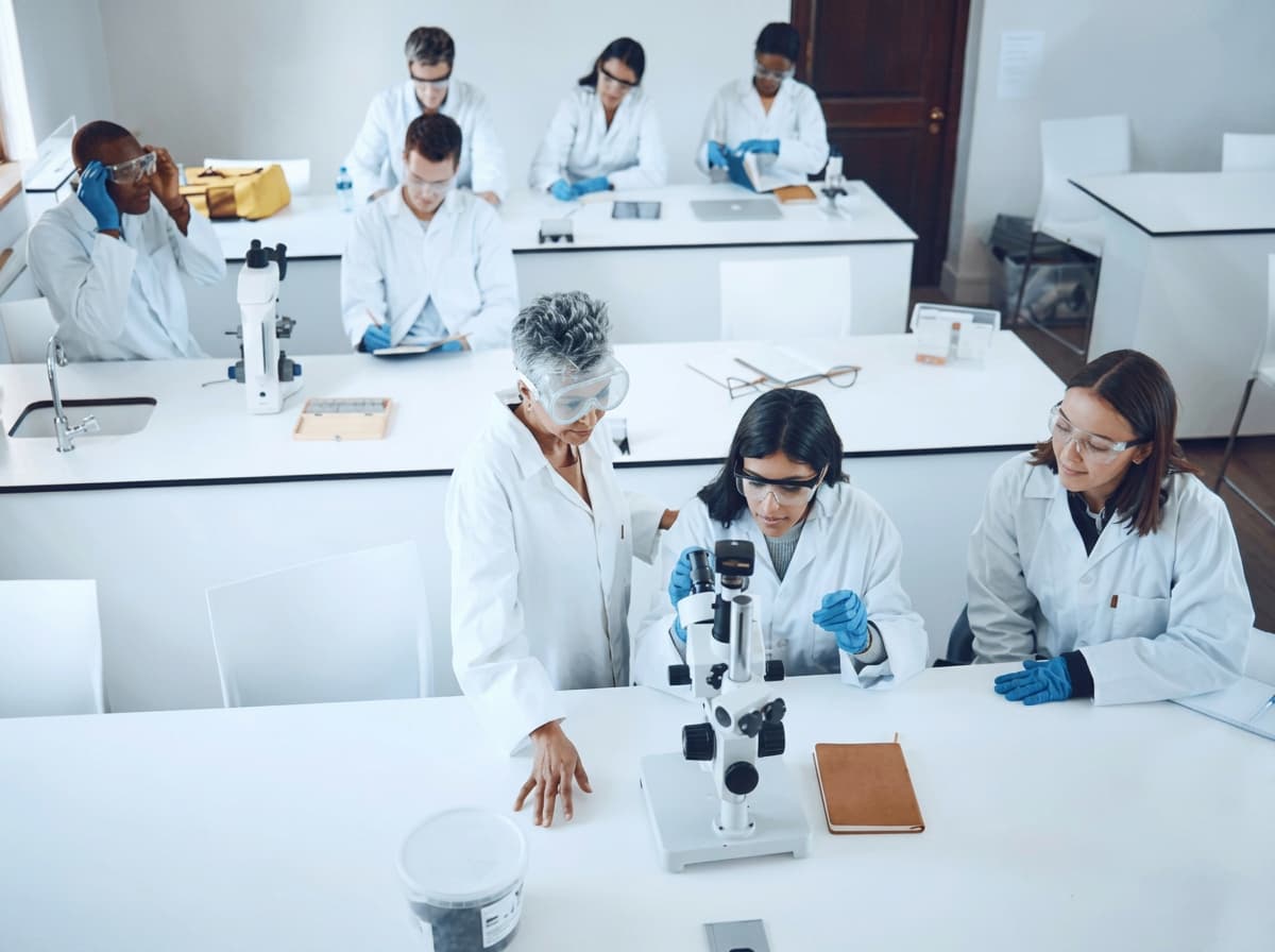 An overhead view of a science laboratory where students in lab coats work at a microscope.