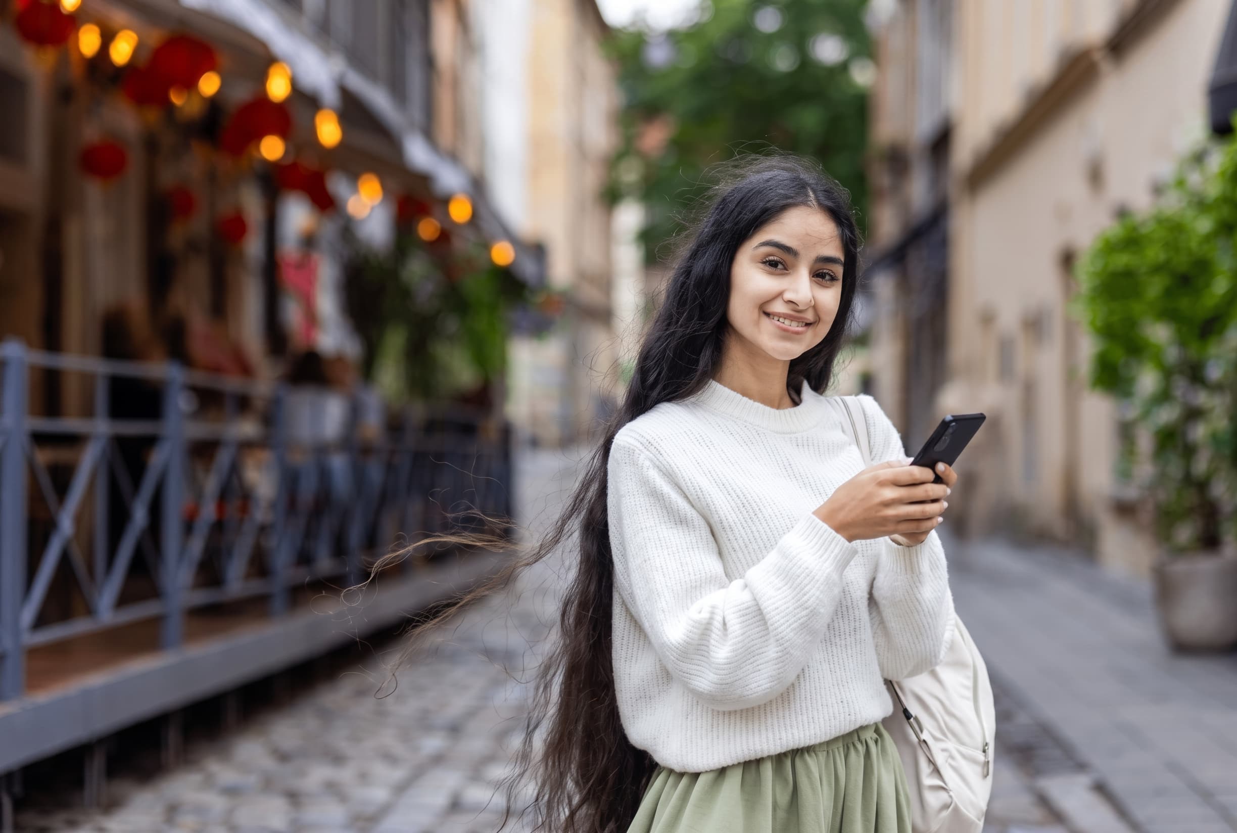 A student walking along an old European street lined with cafés and hanging lanterns.